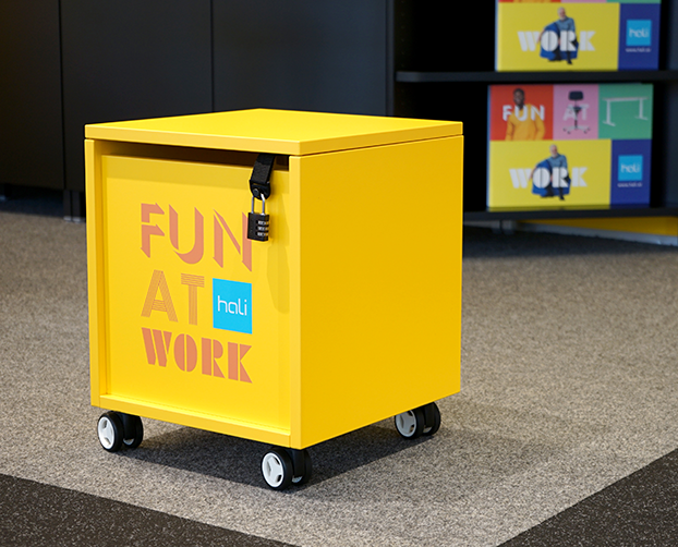 Gelber Bully mit Schloss und „FUN AT WORK“-Slogan im hali Showroom
