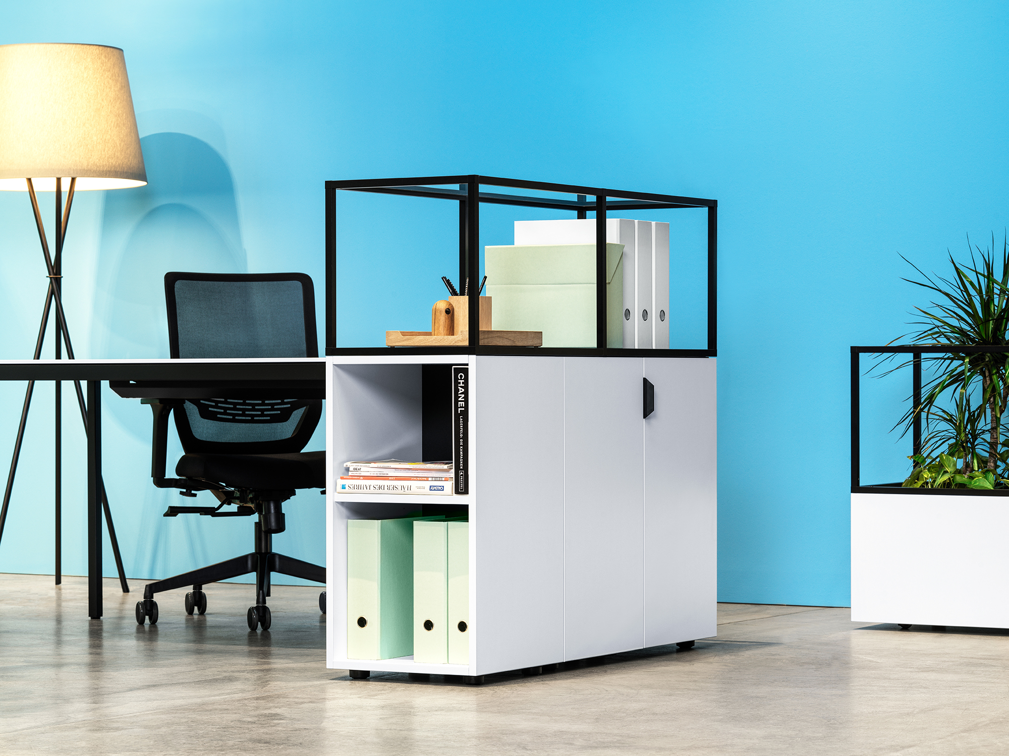 Büroarbeitsplätze mit grünen Containern, Regalen und Sichtschutzwänden vor blauer Backsteinwand