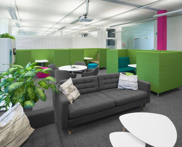 Graues Sofa mit Zierkissen in Lounge-Atmosphäre, umgeben von Rückzugsboxen und Grünpflanzen