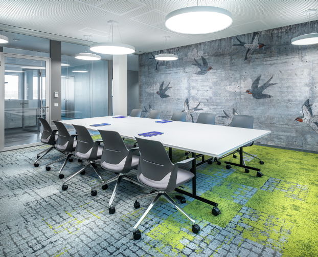Moderner Meetingraum bei Fressnapf mit Vogel-Wandgrafik, hellem Tisch und grüner Teppichzone