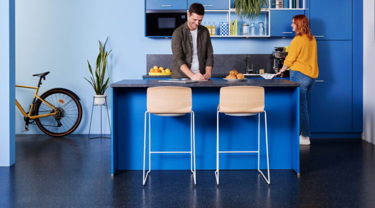 Zwei Curve Barhocker mit Holzsitzschale und Kufengestell an Hochtisch in moderner Büroküche.