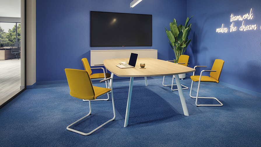 Vier Curve Besucherstühle mit Armlehnen um Konferenztisch in modernem Meetingraum.