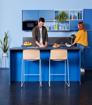 Curve Barhocker mit Holzsitzschale und weißem Kufengestell an blauem Hochtisch.