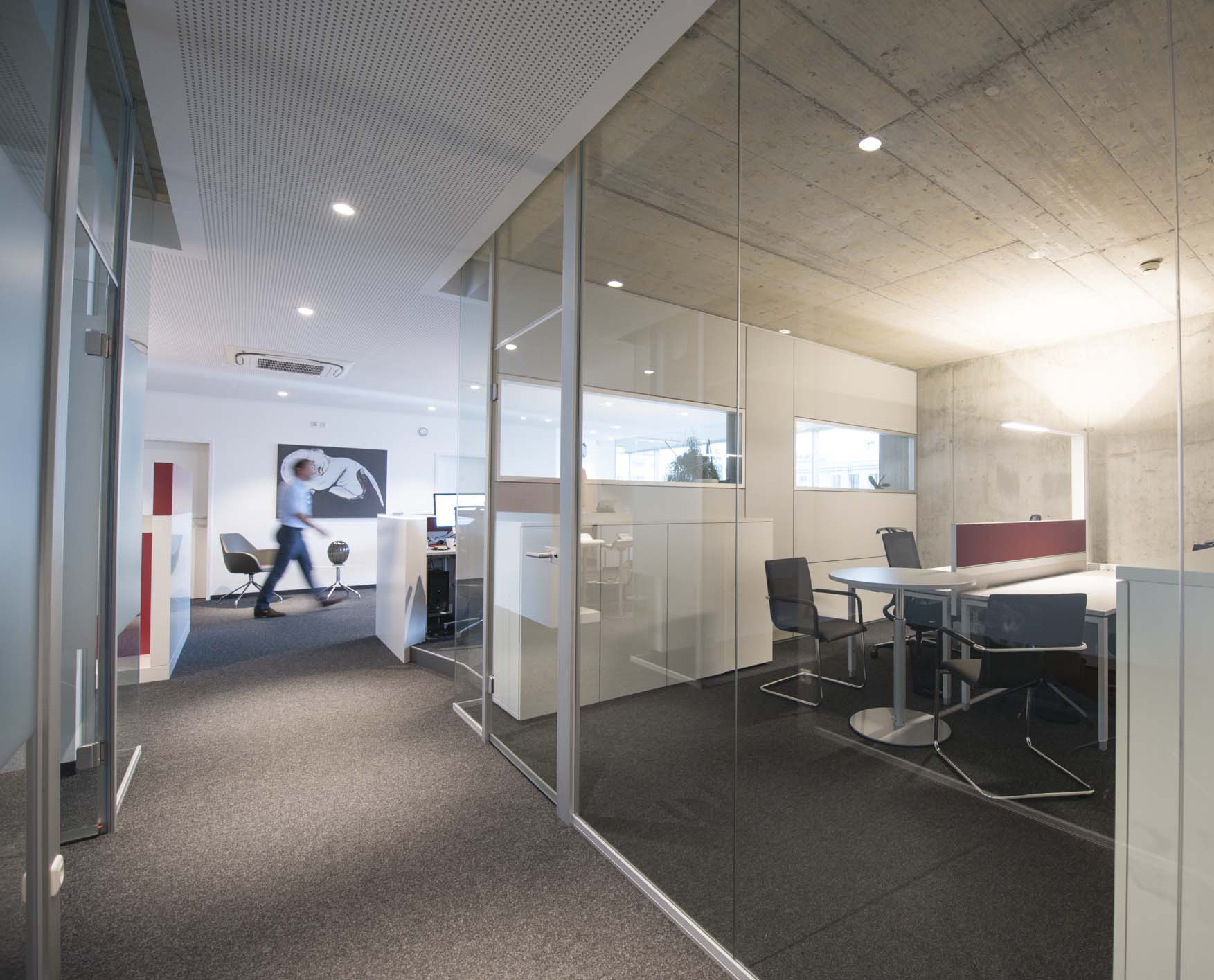 Offener Büroflur mit Glaswänden, Einblick in Arbeitsplatzbereich mit Schreibtisch und Stauraum