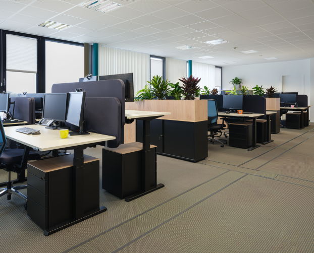 Großraumbüro mit mehreren Arbeitsplätzen, Monitoren, Stauraummodulen und integrierten Pflanzenelementen.